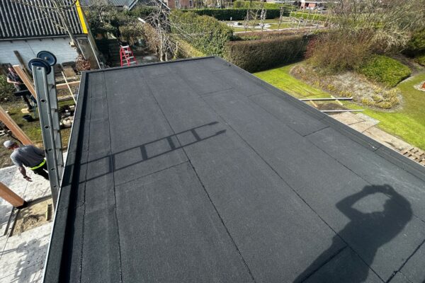 Het platte dak van een terrasoverkapping met een nieuwe bitumen toplaag