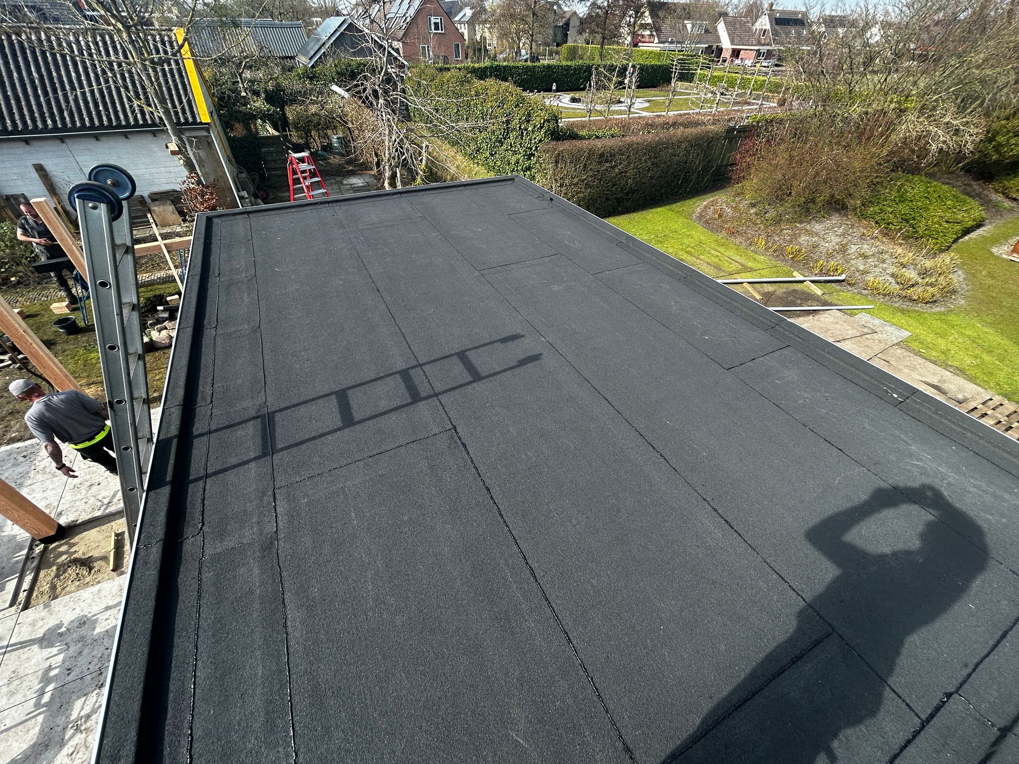 Het platte dak van een terrasoverkapping met een nieuwe bitumen toplaag