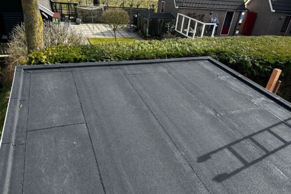 Het platte dak van een terrasoverkapping met een nieuwe bitumen toplaag afgewerkt met een aluminium trim